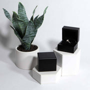 lifestyle photo of black wood ring box on hexagon stands with diamond ring 