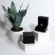 lifestyle photo of black wood ring box on hexagon stands with diamond ring