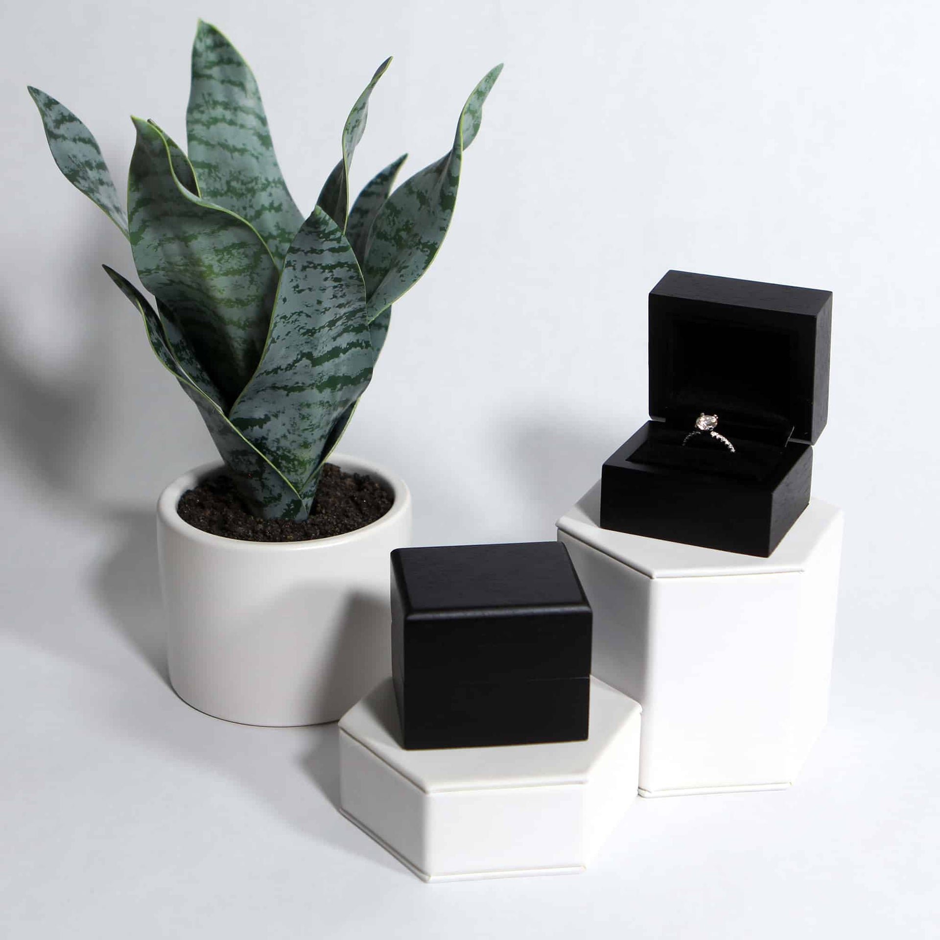lifestyle photo of black wood ring box on hexagon stands with diamond ring