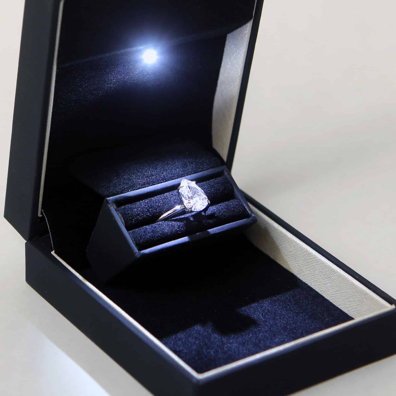 beautiful pear shaped large diamond ring in a slim black ring box with contrasting stripe and LED light