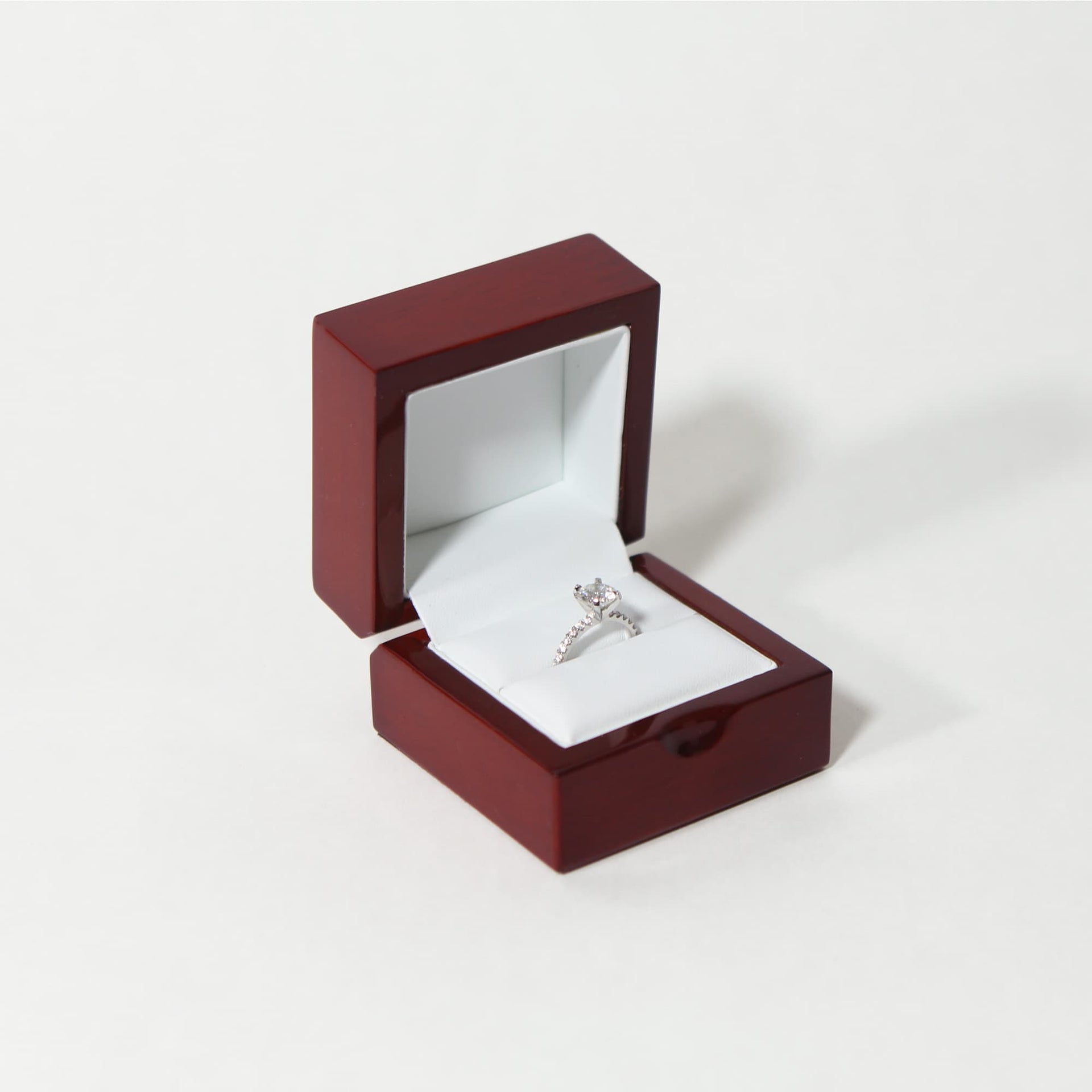 glossy single slot rosewood ring box with white leather interior with a diamond engagement ring inside